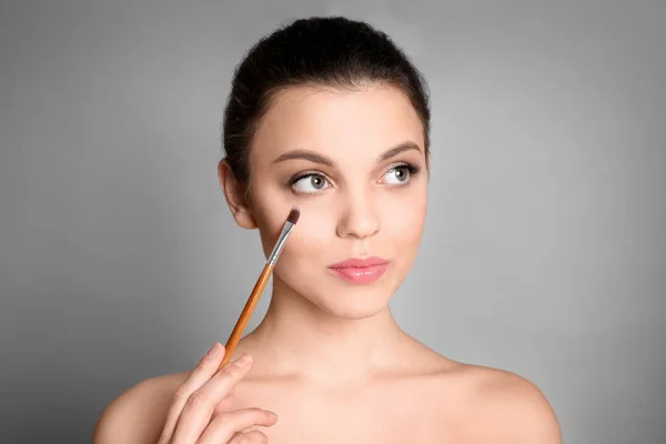 Mujer joven que aplica maquillaje sobre fondo gris. Productos cosméticos profesionales — Foto de Stock