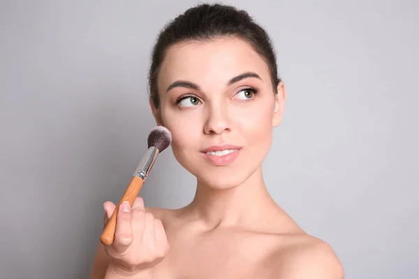 Ung kvinna tillämpa makeup på grå bakgrund. Professionella kosmetiska produkter — Stockfoto