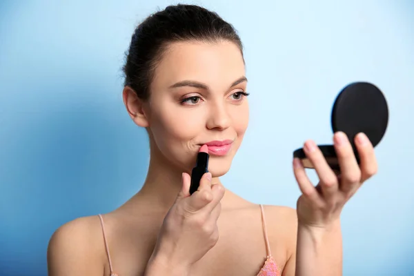 Ung kvinna applicera läppstift på färgbakgrund. Professionell makeup produkter — Stockfoto
