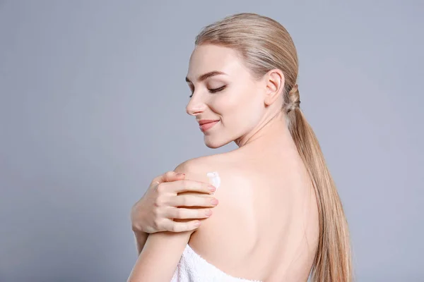 Young woman applying body cream on color background — Stock Photo, Image