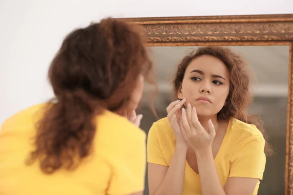 Mooie jonge vrouw met acneprobleem kijken in de spiegel thuis — Stockfoto