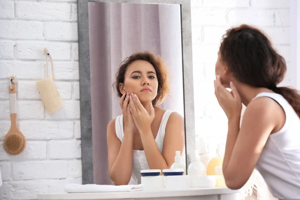 Mooie jonge vrouw met acneprobleem kijken in de spiegel thuis — Stockfoto