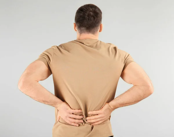 Young man suffering from back pain on light background — Stock Photo, Image