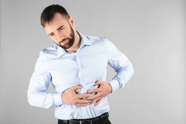 Hombre joven que sufre de dolor abdominal sobre fondo claro — Foto de Stock