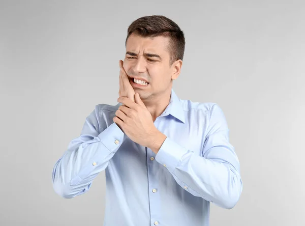 Jovem sofrendo de dor de dente no fundo claro — Fotografia de Stock