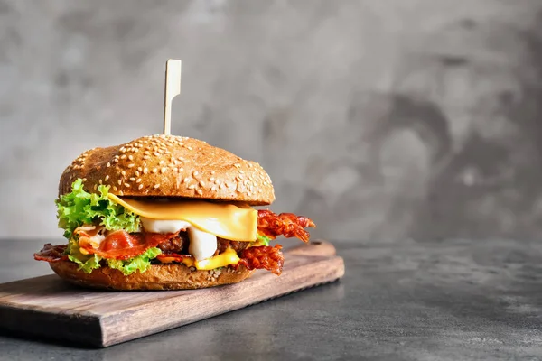 Hambúrguer saboroso com bacon na placa de madeira — Fotografia de Stock