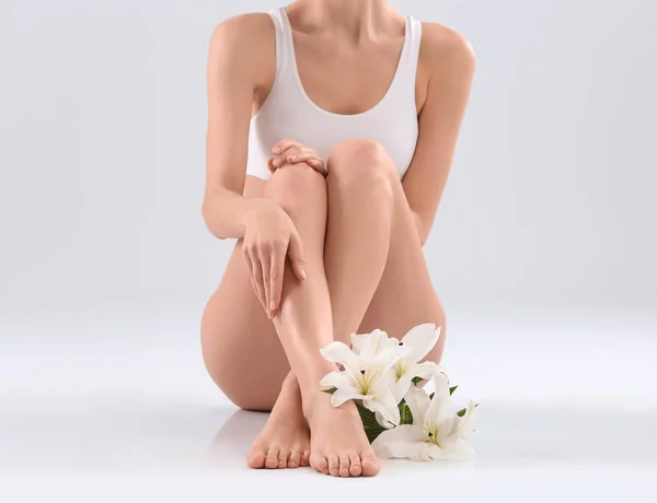 Young woman with beautiful silky body and flowers on light background — Stock Photo, Image