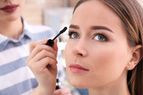 Professional visage artist applying makeup on woman's face in salon, closeup