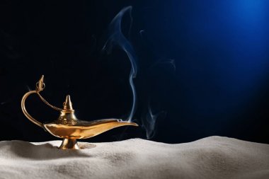 Aladdin magic lamp on sand against dark background clipart