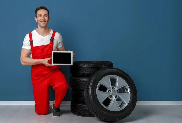 Mladí mechanik v uniformě s tablet Pc a automobilové pneumatiky barevné zdi — Stock fotografie