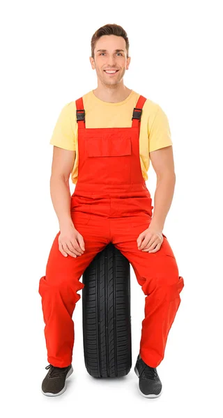 Jovem mecânico em uniforme com pneu de carro no fundo branco — Fotografia de Stock