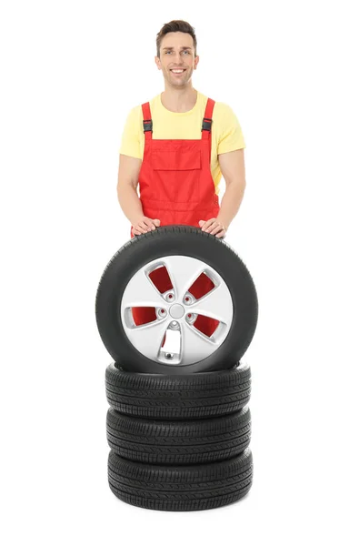 Молодой механик в форме с автомобильными шинами на белом фоне — стоковое фото