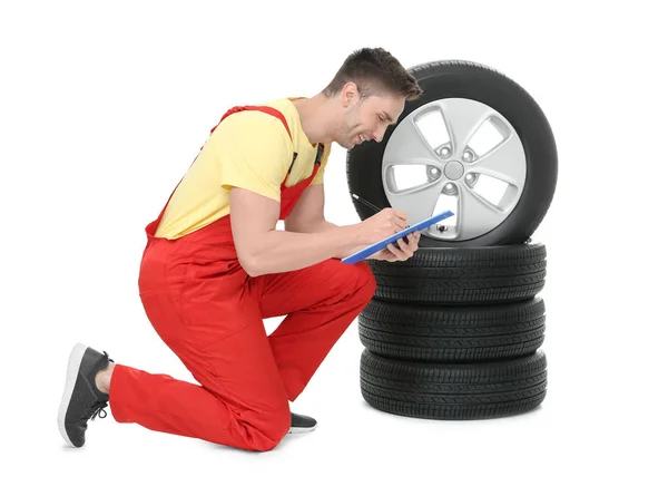 Jovem mecânico de automóveis com prancheta e pneus de carro no fundo branco — Fotografia de Stock