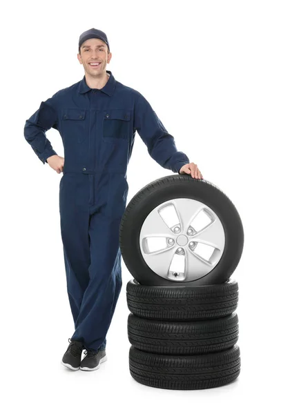Молодой механик в форме с автомобильными шинами на белом фоне — стоковое фото