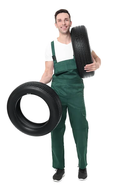Jovem mecânico em uniforme segurando pneus de carro no fundo branco — Fotografia de Stock