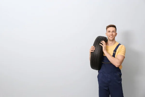 Mecánico masculino con neumático de coche sobre fondo claro —  Fotos de Stock