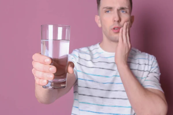 Hombre joven con dientes sensibles y vaso de agua fría sobre fondo de color — Foto de Stock