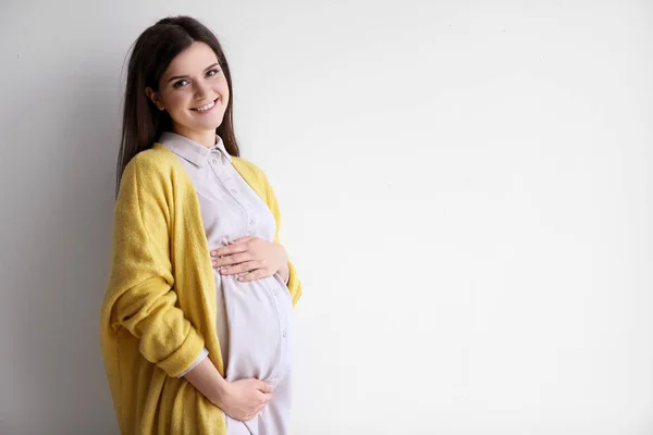 Młoda kobieta w ciąży w ubranie na jasnym tle — Zdjęcie stockowe