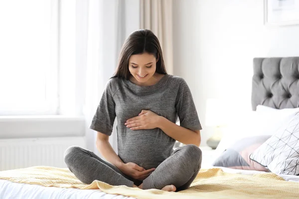 Giovane donna incinta seduta sul letto a casa — Foto Stock