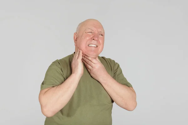 Hombre mayor que sufre de dolor de garganta en un fondo claro. Dolor duradero —  Fotos de Stock