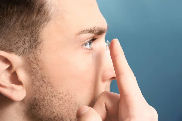Junger Mann nimmt Kontaktlinse vor farbigem Hintergrund ins Auge — Stockfoto