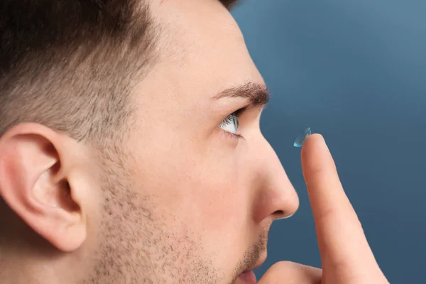 Junger Mann nimmt Kontaktlinse vor farbigem Hintergrund ins Auge — Stockfoto