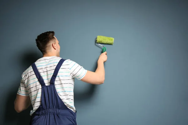 Joven decorador masculino con rodillo de pintura cerca de la pared de color — Foto de Stock