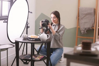 Profesyonel kameralı genç bir kadın stüdyoda yemek fotoğrafı çekiyor.
