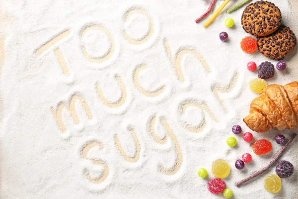 Composition with sweets and phrase TOO MUCH SUGAR written on sugar sand — Stock Photo, Image