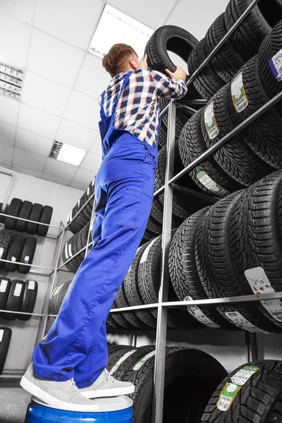 Jovem mecânico masculino com pneus de carro no centro de serviços de automóveis — Fotografia de Stock