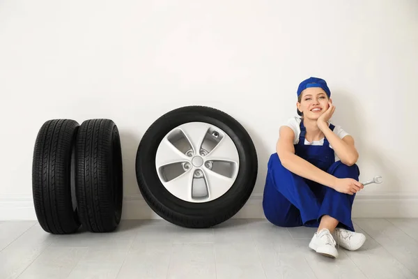 Mecânico feminino com pneus de carro no fundo da parede leve — Fotografia de Stock