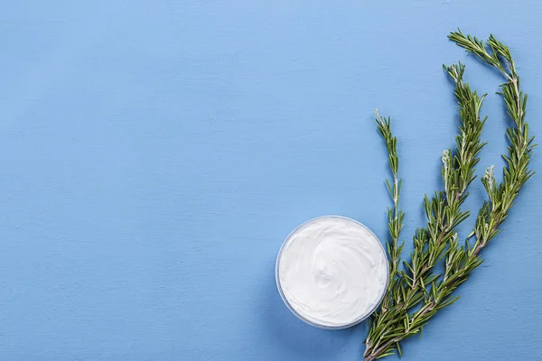 Jar with body care cream and rosemary on color background