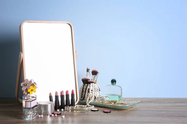 Elegante espejo, productos de maquillaje y accesorios en la mesa cerca de la pared de luz — Foto de Stock