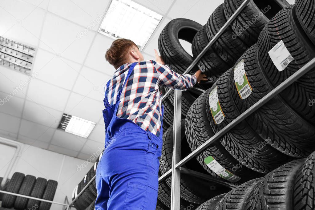 Young male mechanic with car tires in automobile service center