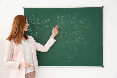 Güzel genç öğretmen sınıfta yazı tahtası üzerinde yazılı matematik formüller açıklayan