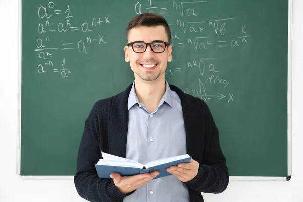 Young male teacher with book standing in classroom