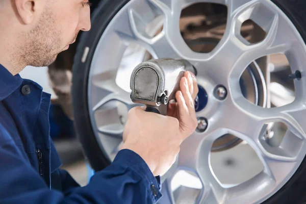 Joven mecánico cambiando de rueda en el servicio de neumáticos — Foto de Stock