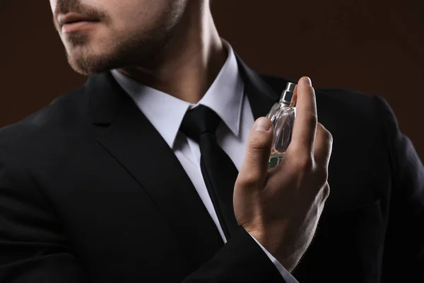 Hombre guapo en traje usando perfume sobre fondo oscuro, primer plano — Foto de Stock