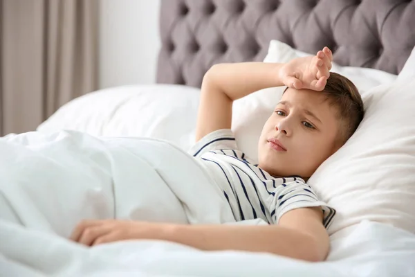 Маленький хлопчик страждає від головного болю, лежачи в ліжку вдома — стокове фото