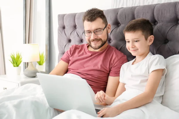 Kleine jongen en zijn papa met laptop in slaapkamer — Stockfoto