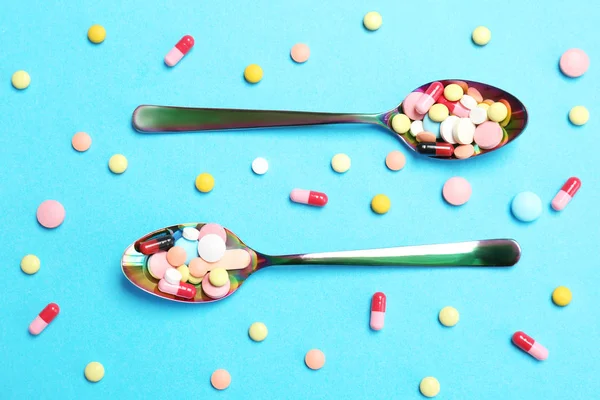 Cucchiai e diverse pillole su sfondo a colori — Foto Stock
