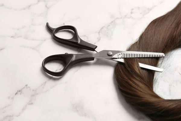 Forbici professionali da parrucchiere e ciocca di capelli castani su fondo marmo — Foto Stock