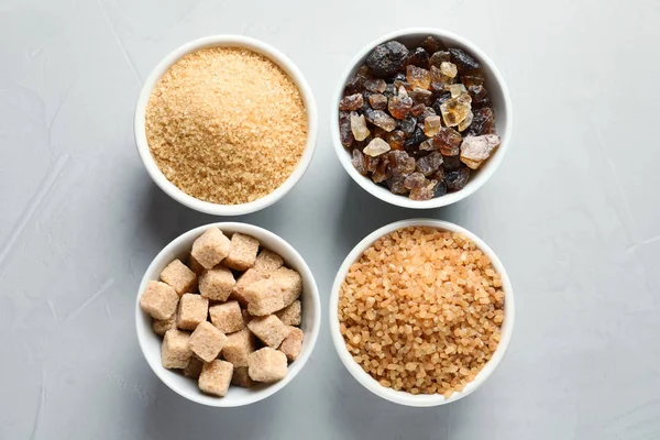 Bowls with different types of sugar on gray background — Stock Photo, Image