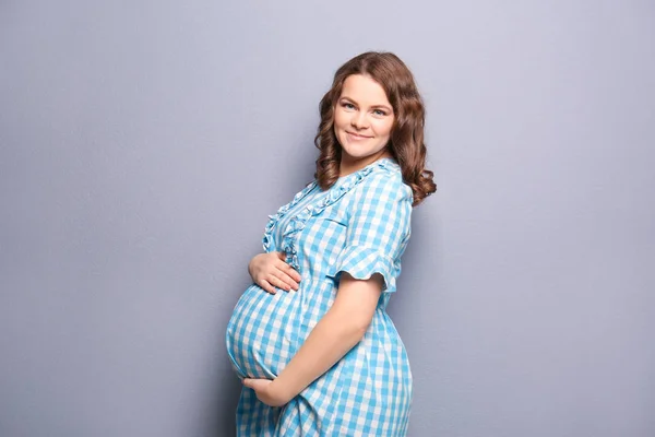 Молода вагітна жінка в повсякденному одязі на сірому фоні — стокове фото