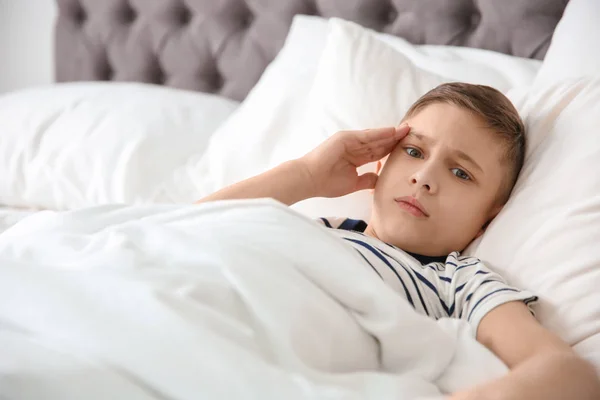 Мальчик страдает от головной боли, лежа дома в постели. — стоковое фото