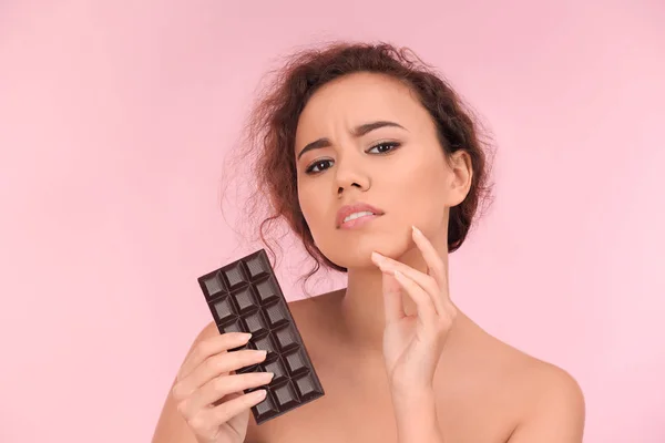 Mooie jonge vrouw met acneprobleem houden van chocolade op kleur achtergrond. Allergie huid — Stockfoto