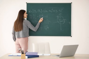 Genç kadın öğretmen sınıfta yazı tahtası üzerinde yazma