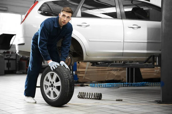 Jovem mecânico com pneu de carro no centro de serviço — Fotografia de Stock