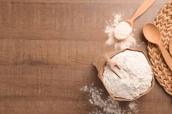 Bolsa de papel y cuchara con harina sobre fondo de madera, vista superior — Foto de Stock