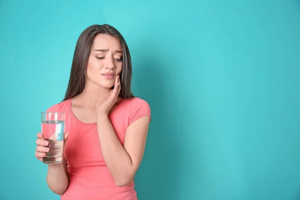 Frau mit empfindlichen Zähnen hält Glas Wasser auf farbigem Hintergrund — Stockfoto